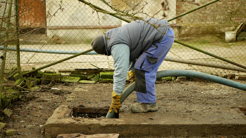 Man standing over a septic tank and pumping it with a hose