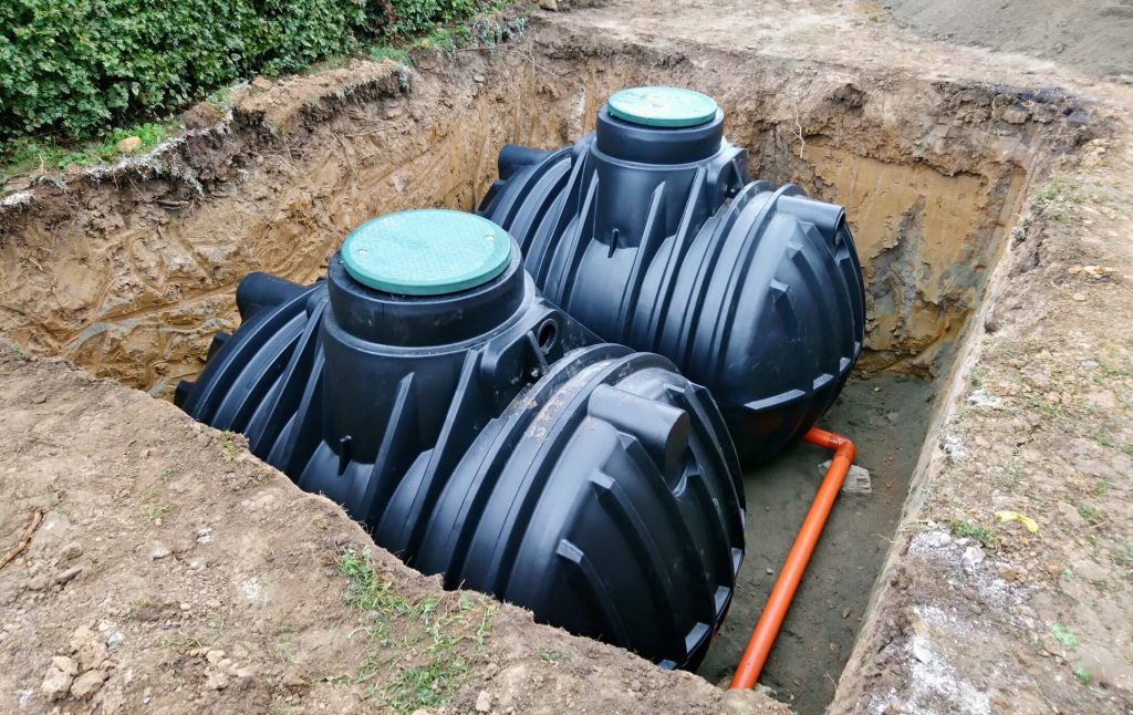 2 black septic tankss that are placed in a large whole in the ground both next to each other