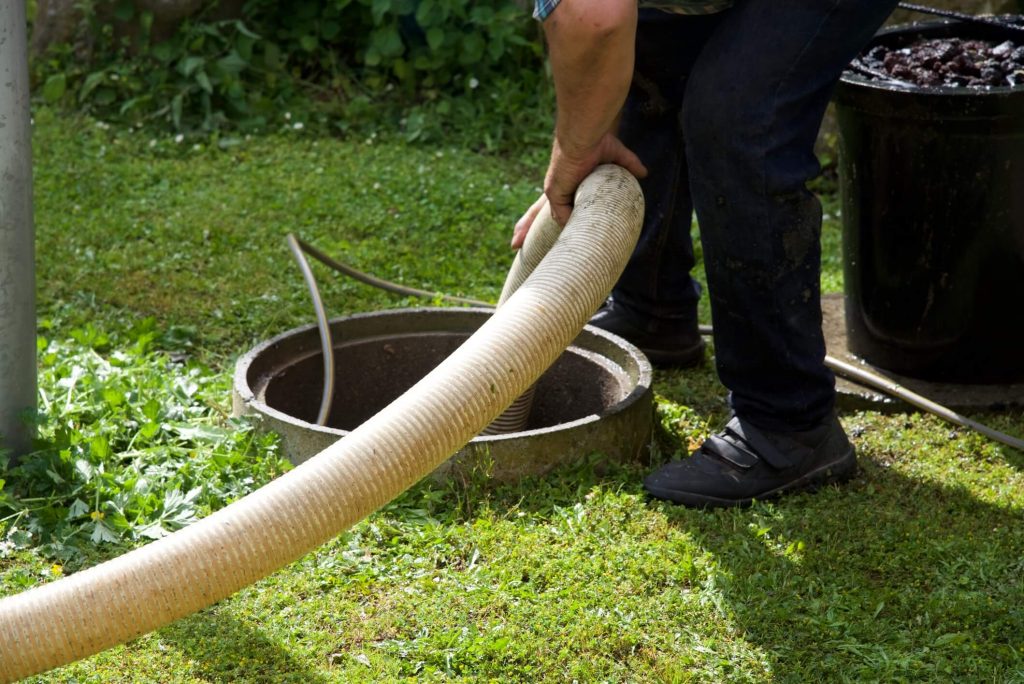Man emptying a septic tank using a long white hose.